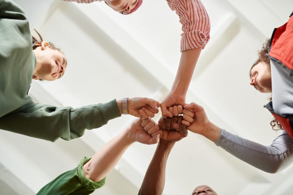 Four diverse team members join fists together, displaying unity and teamwork.